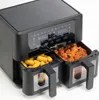 A close-up, slightly angled view of a black dual-basket air fryer with food in both baskets. The digital display is visible at the top. Produktbild-Vorschau
