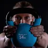 A person is holding a blue kettlebell in front of their face against a dark background. Podgląd zdjęcia produktu