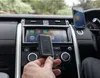 A person holding a black device in a car, with the car's infotainment screen and a smartphone visible. Náhľad obrázku produktu