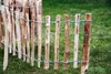 A close-up view of a rustic wooden fence made of natural branches, set against a green grassy background. Produktbild-Vorschau