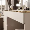 Close-up of a white vanity table with gold trim, showing drawers and some makeup items. Produktbild-Vorschau