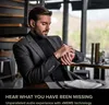 A man wearing a suit and earbuds is looking at his watch in a modern setting. Produktbild-Vorschau