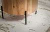 Close-up of the base of a round wooden table with black metal legs, resting on a patterned rug. Produktbild-Vorschau