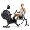 A woman is using a black and gray rowing machine indoors against a white background. Produktbild-Vorschau