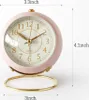 A pink alarm clock with gold accents is shown on a white background, with dimensions indicated by text. Produktbild-Vorschau