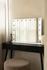 A vanity mirror with lights is placed on a black vanity table, with a stool in front. Produktbild-Vorschau