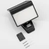 A black solar-powered outdoor light with a motion sensor is shown on a white background, along with its mounting bracket, screws, and wall plugs. Produktbild-Vorschau
