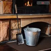 A fireplace hearth with a metal bucket and a shovel next to it, with a fire burning in the background. Produktbild-Vorschau