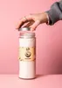 A hand is shown opening a jar of coconut oil against a pink background. Produktbild-Vorschau