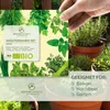 A hand holding a product package with images of herbs and plants, with potted herbs in the background. Náhled obrázku produktu