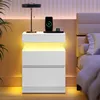 A modern white nightstand with integrated lighting is placed next to a bed. Produktbild-Vorschau