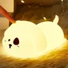 A finger is touching a cute, glowing puppy-shaped night light that is lying on a fluffy rug. Fairy lights are visible in the background. Produktbild-Vorschau
