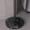 The base of a black floor lamp with a black and white marble pattern is shown on a gray floor. A gray wall is in the background. Produktbild-Vorschau