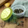 A close-up of a clear plastic food container with a green lid, filled with pumpkin seeds, placed on a wooden surface with a fallen leaf and a cloth in the background. Náhľad obrázku produktu