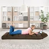 A woman is lying on a brown floor chair and using a laptop in a living room with shelves in the background. Náhľad obrázku produktu