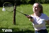 A young woman playing badminton outdoors in a grassy area. Produktbild-Vorschau