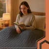 A woman is reading a book in bed, under a blanket. Produktbild-Vorschau
