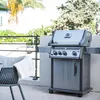 A gas grill is shown on an outdoor patio with a chair and a throw blanket. Produktbild-Vorschau