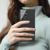 A person's hand holding a smartphone with a camera lens protector. Produktbild-Vorschau