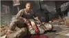A scene from a video game depicting two men, one injured and being tended to by another, with other figures and debris in the background. Produktbild-Vorschau
