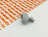 A gray plastic part is placed on a white surface next to a sheet of packaging material with orange text. Produktbild-Vorschau