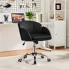 A black office chair is shown in a home office setting, with a desk, laptop, and shelves in the background. Produktbild-Vorschau