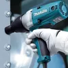 A person wearing white gloves is using a teal and gray Makita impact wrench to tighten a bolt on a metal surface. Podgląd zdjęcia produktu