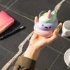A hand holding a colorful stress toy on a dark patterned surface, with a notebook and pen in the background. Voir les images du produit