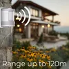 A motion sensor is mounted on a stone wall in front of a house with flowers in the foreground. Anteprima dell’immagine prodotto