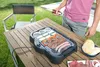 A person is grilling food on an electric grill on a wooden table outdoors. Náhled obrázku produktu