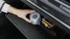 A hand is placing a portable work light into a car's glove compartment next to a box of LED bulbs. Produktbild-Vorschau