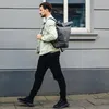 A man walks down a sidewalk carrying a backpack. Anteprima dell’immagine prodotto
