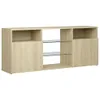 A long, low media console with a light wood grain finish and clear glass shelves, shown against a white background. Náhled obrázku produktu