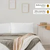 A bed with pillows and blankets, next to a nightstand with books. Produktbild-Vorschau