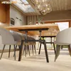 A dining table with black metal legs and a wooden top, set in a modern dining room with chairs and a chandelier. Produktbild-Vorschau