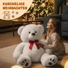 A young girl is sitting on the floor next to a large white teddy bear in a living room decorated for Christmas. Anteprima dell’immagine prodotto
