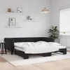 A black velvet sofa bed is shown in a room with white walls and wooden floors. The sofa bed is extended and made up with white bedding. Produktbild-Vorschau
