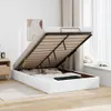 A white ottoman bed with the storage compartment open, revealing wooden slats and bedding inside. The bed is in a room with light wooden flooring and sheer curtains in the background. Produktbild-Vorschau