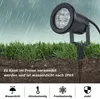 A black LED garden spotlight is shown planted in the ground with grass around it, under a simulated rainy sky. Produktbild-Vorschau