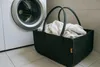 A dark gray felt basket filled with white laundry sits on a tiled floor next to a white washing machine. Náhled obrázku produktu
