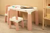 A child's table and two chairs are set up in a room with a light-colored wall and wooden floor. Produktbild-Vorschau