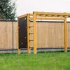 An outdoor gym structure with a climbing wall and monkey bars, set against a wooden fence and green grass. Anteprima dell’immagine prodotto