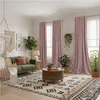 A cozy living room with a green sofa, macrame hanging chair, patterned rug, and pink curtains. Voir les images du produit