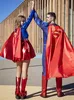 Two people dressed as Superman and Supergirl giving each other a high five in front of a modern building. Produktbild-Vorschau