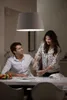 A couple is at a table, with the woman pouring water into a glass. A pendant light hangs above them. Produktbild-Vorschau