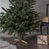 A Christmas tree with lights and a stand, with wrapped gifts nearby. Produktbild-Vorschau