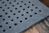 A close-up of a square cast iron grate with evenly spaced holes, resting on a wooden surface. Voir les images du produit
