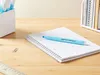 A light blue marker pen lies on a white grid notebook on a wooden desk. Produktbild-Vorschau
