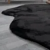 A close-up shot of a black, fluffy rug with an irregular shape, lying on a light gray wooden floor. Produktbild-Vorschau