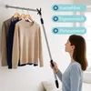 A woman is using a telescopic pole with a hook to reach clothes on a hanging rack. The scene is indoors, likely a closet or bedroom. Produktbild-Vorschau